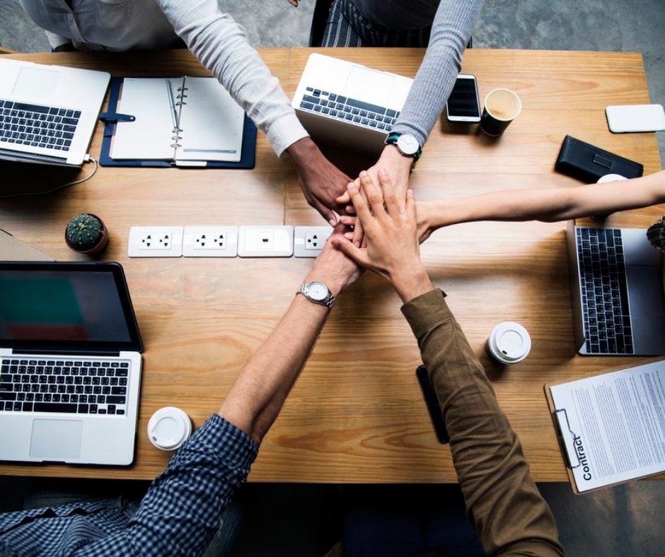 A group of workers putting their hands together over a work table.