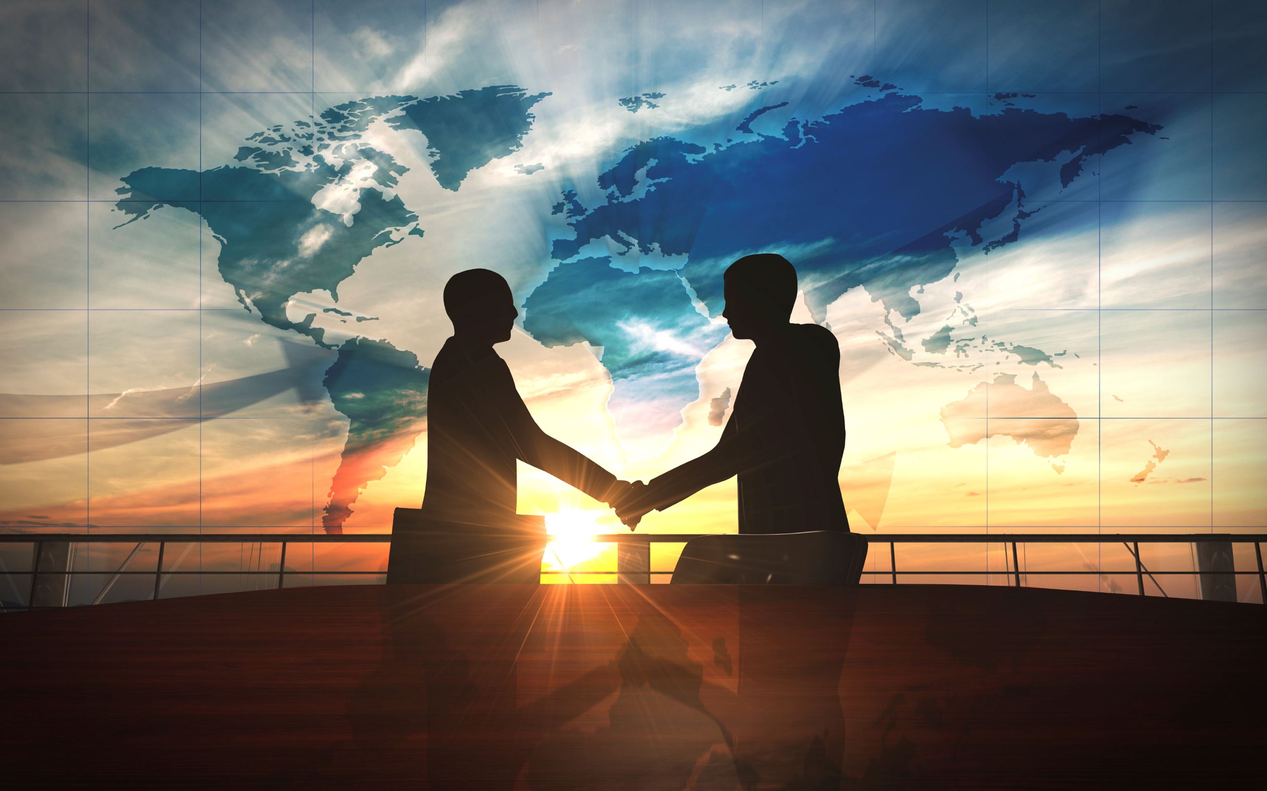 Two businessmen silhouettes shake hands with a sunset background behind them.